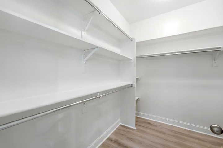 Walk-in closet featuring built-in shelving, chrome hanging rods, and wood-finish flooring