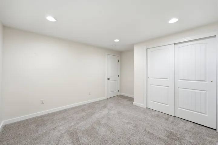 Plush gray carpeting, white walls, recessed ceiling lighting, a white panel door, and white sliding closet doors with arched top panels