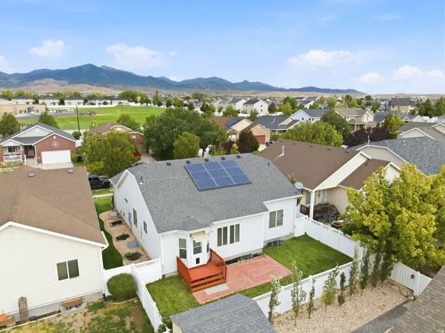 Rear exterior with solar panels, a red-stained deck, a bay window, and a fenced backyard featuring a red brick patio and a lawn