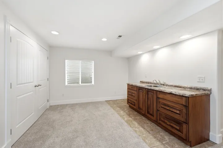 Recessed lighting, wood-finish cabinetry, dual sinks, stone-finish countertop, and tiled flooring