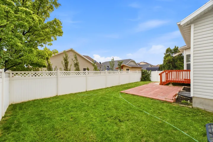 Expansive private backyard featuring a manicured lawn, white lattice-top fencing, and a red paver patio with a matching red-stained wood deck