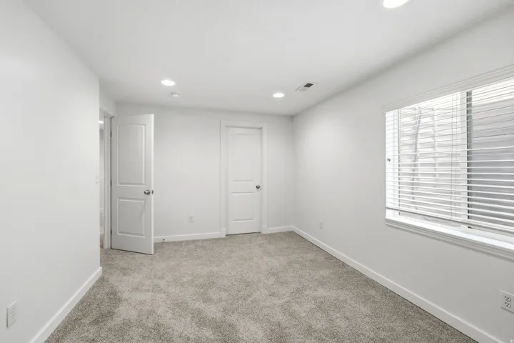 Neutral-toned carpeting, white walls, recessed lighting, and a white-framed window with blinds