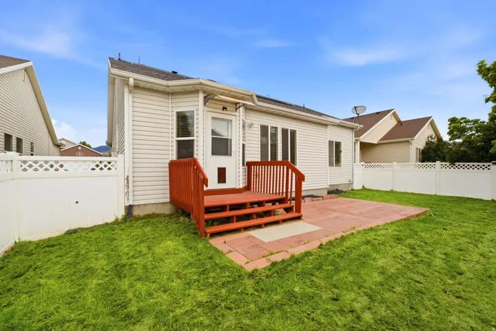 Rear exterior featuring horizontal siding, a red-stained wooden deck, a red brick-patterned patio, and white lattice-top fencing