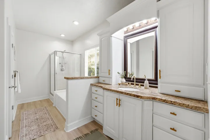 White cabinetry with gold-finish hardware, light wood-finish flooring, and a walk-in shower with a glass enclosure
