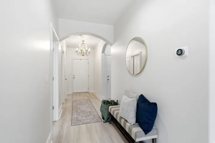 White interior walls, arched entryway, wood-finish flooring, white paneled door, built-in smart thermostat