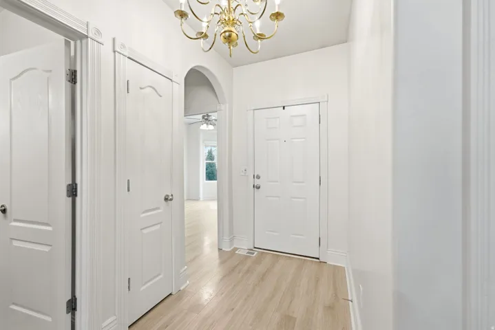 Entryway with wood-finish flooring, a decorative chandelier, white panel doors, and an arched doorway