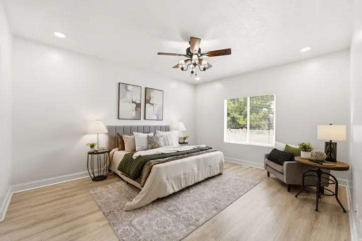 Large Primary bedroom has recessed lighting, wood-finish flooring, a ceiling fan with chandelier lighting, and a large window with blinds