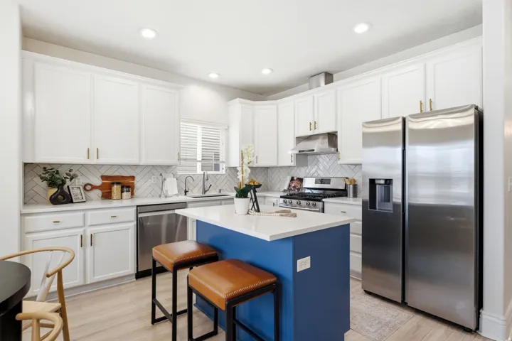 Kitchen featuring white shaker cabinetry, stainless steel appliances, a white herringbone tile backsplash, and a blue kitchen island with a white countertop