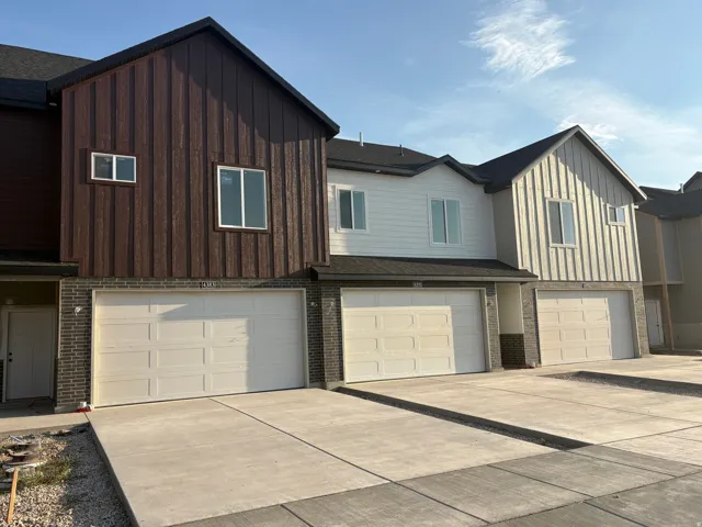 Townhome-style exterior with vertical panel siding, brick veneer accents, white frame windows, and an attached two-car garage