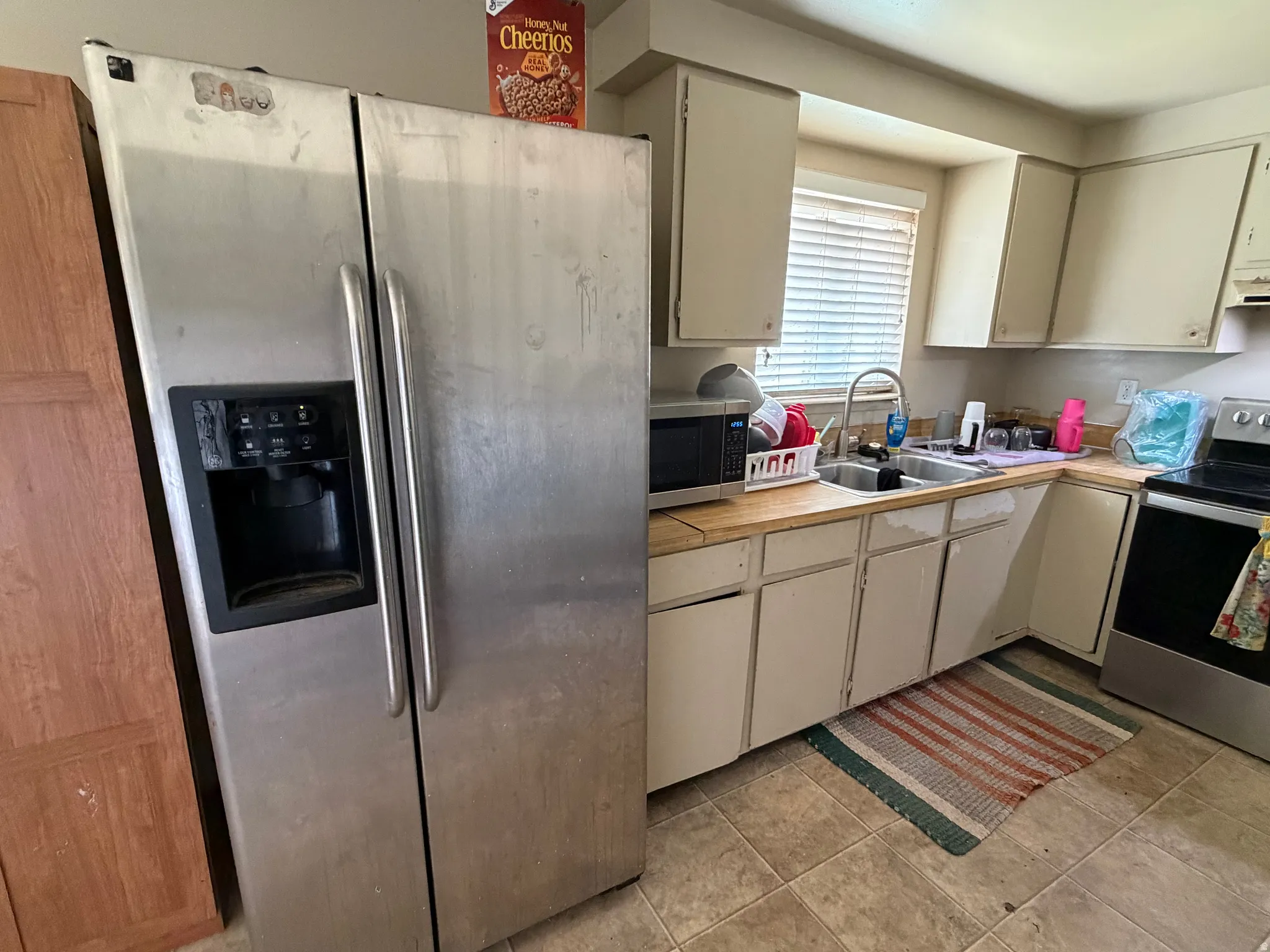Kitchen featuring a stainless steel side-by-side refrigerator, white cabinetry, a double basin sink, and a four-burner electric range