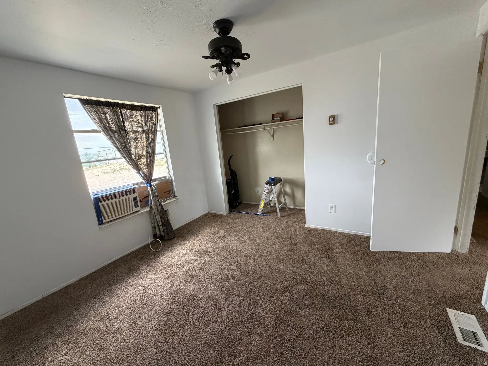 Carpeted flooring, ceiling fan with light fixture, window, and an open closet with a shelving unit