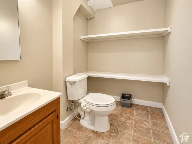 Powder room featuring a wood-finish vanity with an integrated sink, polished chrome faucet, white toilet, and tiled flooring