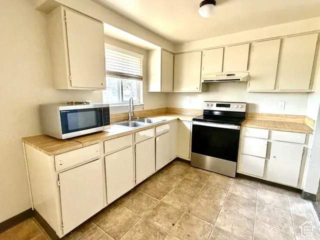 Kitchen with white cabinetry, stainless steel range, wood-finish countertops, and dual basin sink