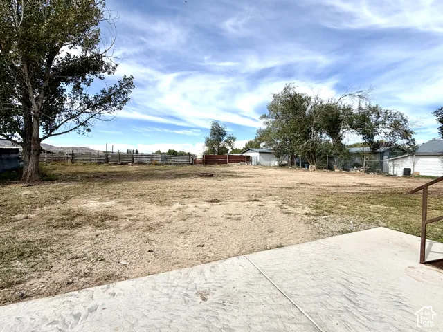 Expansive outdoor space featuring a concrete patio, mature trees, and perimeter fencing