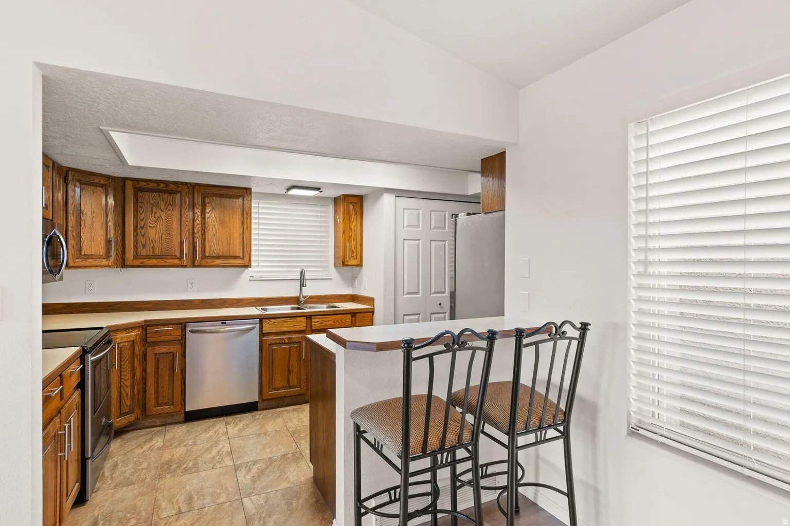 Kitchen featuring wood cabinetry, stainless steel appliances, a double basin sink, and tile flooring