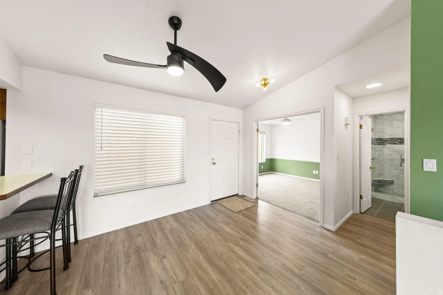 Wood-finish flooring, ceiling fan with integrated lighting, window with blinds, and white entry door