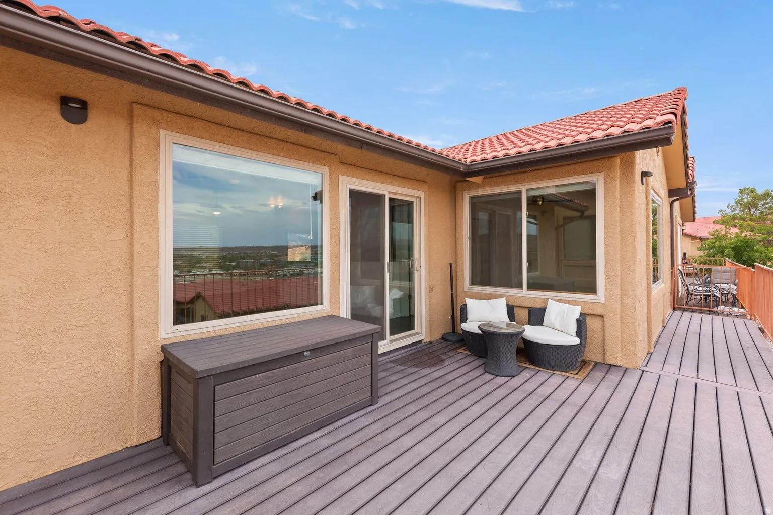 Expansive outdoor deck with composite flooring, stucco exterior, multiple windows, and a sliding glass door
