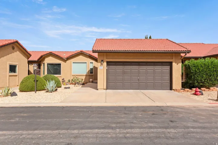Exterior featuring a terra cotta tile roof, attached garage with a panel door, stucco finish, and desert landscaping