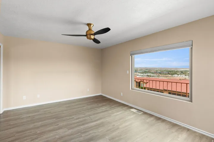 Room featuring wood-finish flooring, a ceiling fan, and a large window with distant scenery