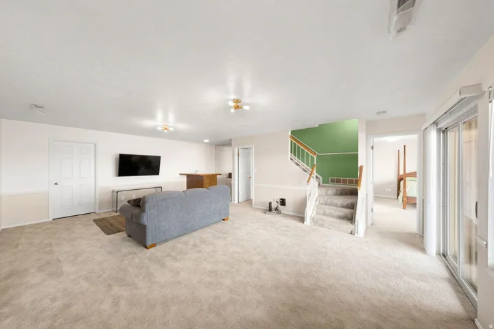 Carpeted flooring throughout, built-in wet bar, interior staircase with green accent wall, and sliding glass door