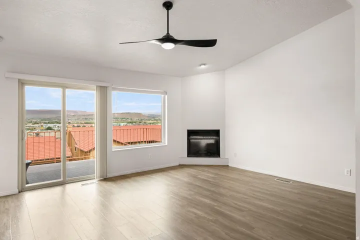 Sliding glass door leading to an exterior balcony, corner-set fireplace, wood-finish flooring, and recessed lighting