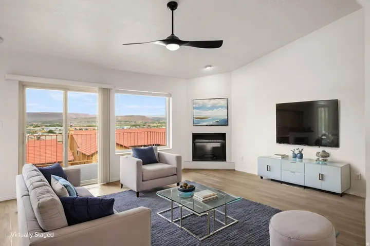Vaulted ceiling with an attached ceiling fan, wood-finish flooring, a corner fireplace, and sliding glass doors