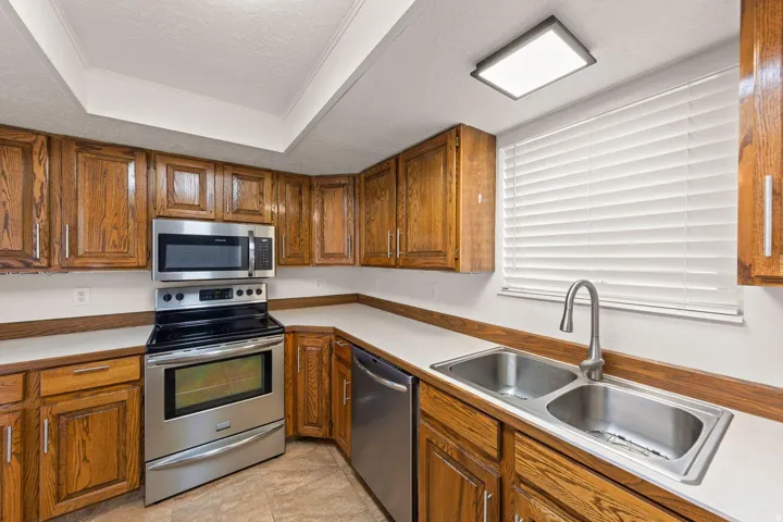 Kitchen featuring wood cabinetry, stainless steel appliances, dual basin sink, and a window with blinds
