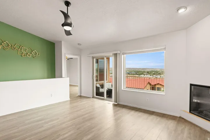 Light wood-finish flooring with a modern ceiling fan, recessed lighting, and a sliding glass door to a balcony