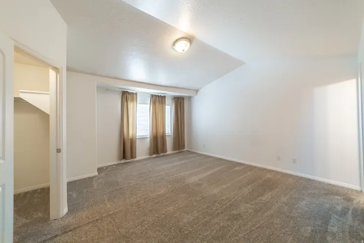 Neutral-toned carpeting, white walls, and a vaulted ceiling