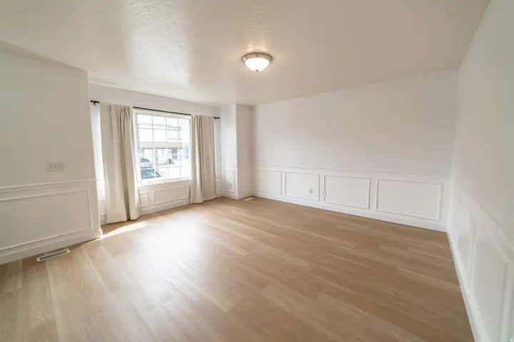 Light wood-finish flooring, white paneled wainscoting, and a prominent window with white trim