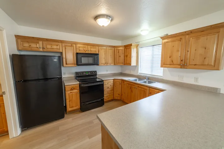 Kitchen featuring wood-finish cabinetry, light-toned countertops, black appliances, and wood-finish flooring