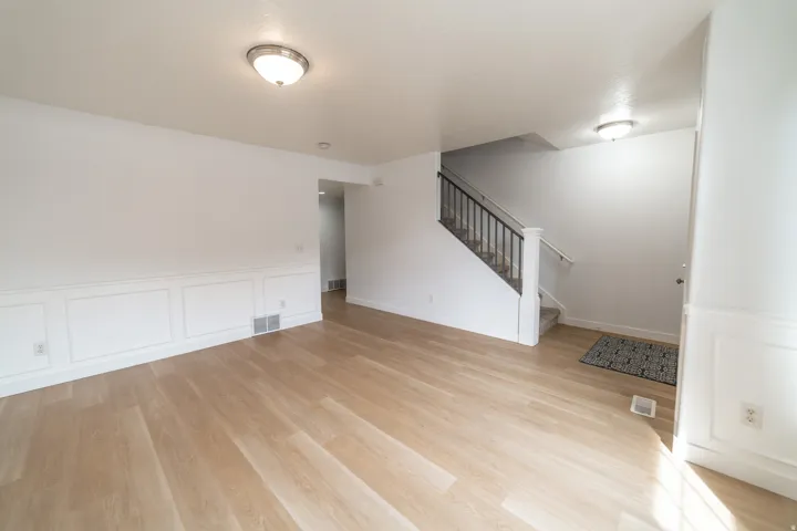 Light wood-finish flooring, white paneled wainscoting, white walls, flush mount ceiling lights, and a staircase with black metal balusters