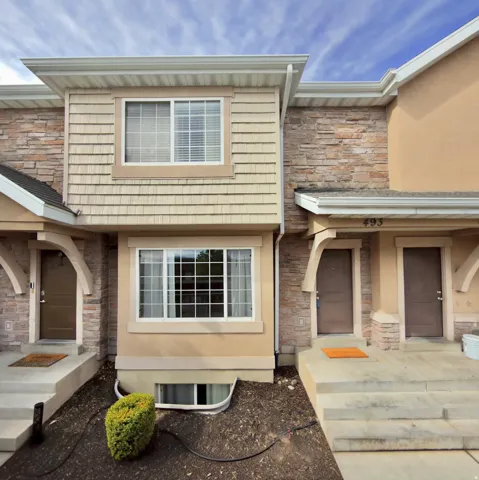 Stone veneer accents, horizontal siding, stucco finish, white-framed windows, and a basement window well