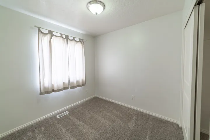 Neutral wall tones, gray carpeting, a window with curtains, and a ceiling-mounted light fixture