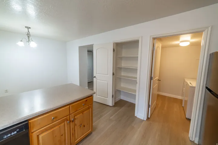 Kitchen island with wood-finish cabinetry and a light-toned countertop, wood-finish flooring, built-in pantry shelving, and an adjacent utility area