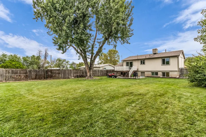 Expansive fenced backyard with a large tree, large grass area and a raised deck with white railings
