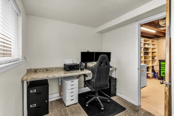 Carpeted room with a built-in desk featuring a stone-finish countertop and a window with blinds