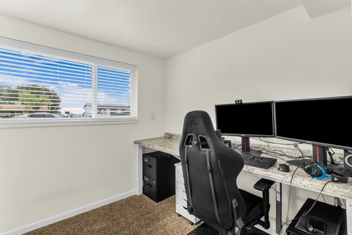 Built-in desk featuring a stone-finish countertop, neutral carpeting, and a window with blinds