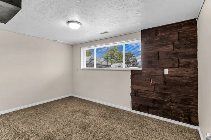 Textured accent wall, neutral carpeting, window with blinds, recessed ceiling light