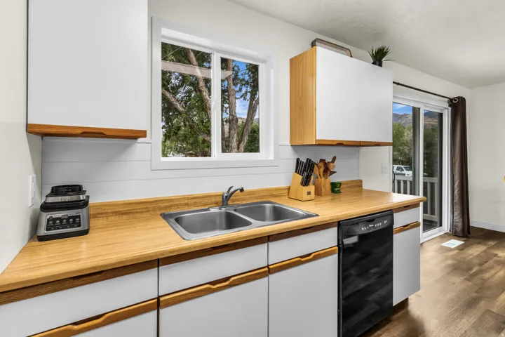 Kitchen featuring wood-finish countertops, white cabinetry with integrated wood-tone handles, a double basin stainless steel sink, and a built-in dishwasher