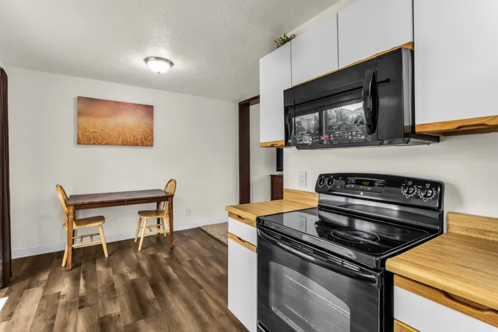 Wood-finish flooring, white cabinetry, black range, black microwave, and light-toned countertops