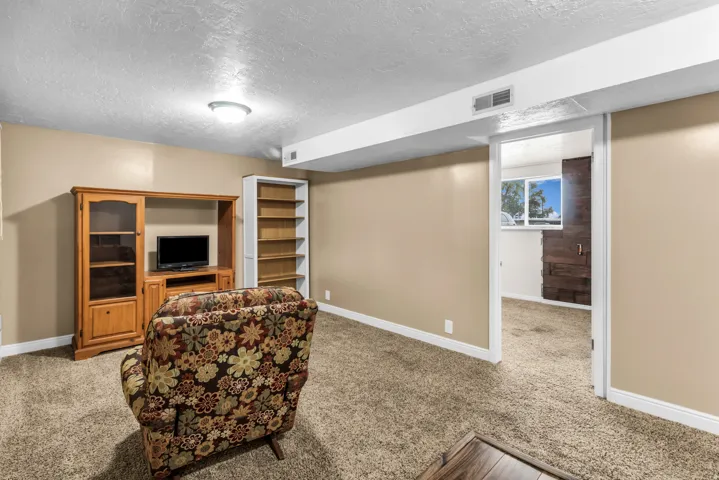 Carpeted flooring, recessed ceiling lighting, built-in shelving, and a doorway opening to an additional bedroom