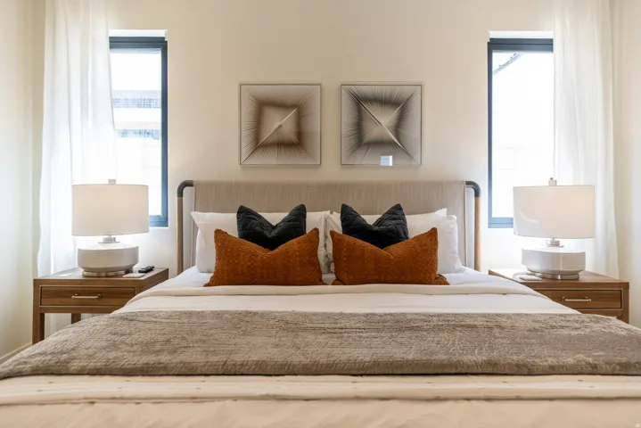 Built-in upholstered headboard with an integrated metal frame, two symmetrical windows with sheer window treatments, and two wood-finish nightstands with single drawers