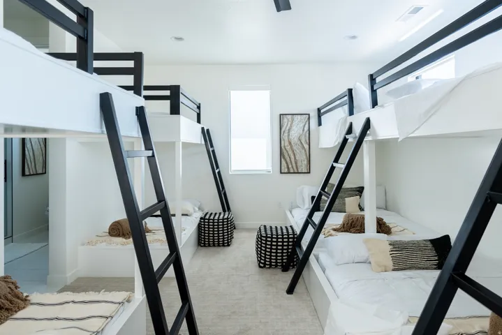 Built-in bunk beds with black metal ladders, white walls, recessed lighting, and a single window