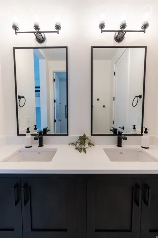 Dual vanity with integrated sinks, white countertops, matte black hardware, dark wood-finish cabinetry, and framed mirrors