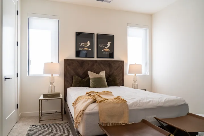 Vertical windows with roller shades, wood-finish headboard, and light-toned carpeting