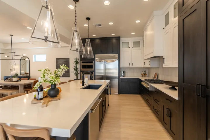 Expansive kitchen island with a built-in sink, stainless steel appliances, two-tone cabinetry, and wood-finish flooring
