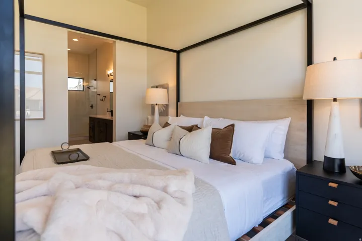 Vaulted ceiling with an open framed bed, light-toned wood-finish headboard, and a dark-toned nightstand