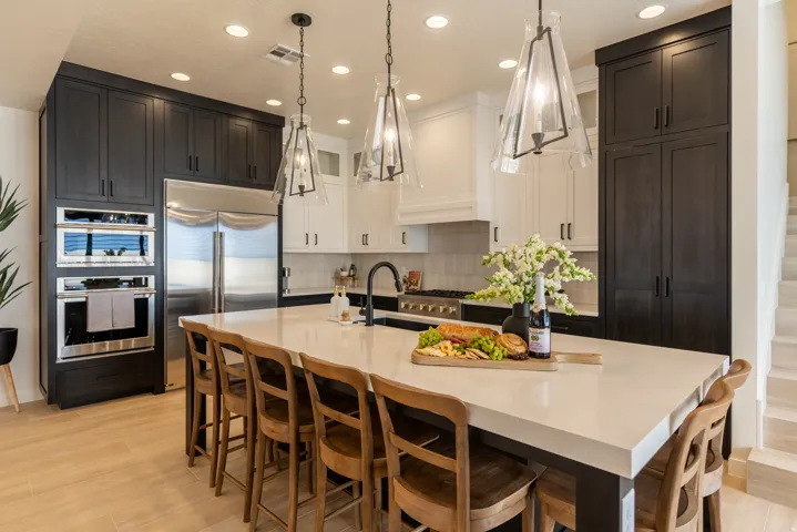 Spacious kitchen featuring a large island with seating, integrated stainless steel appliances, dual-tone cabinetry, and pendant lighting