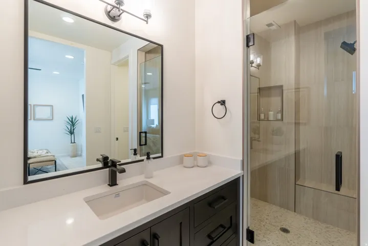 White countertop with integrated sink and matte black faucet, dark wood-finish vanity with ample storage, glass-enclosed shower with built-in bench, and recessed shower niche